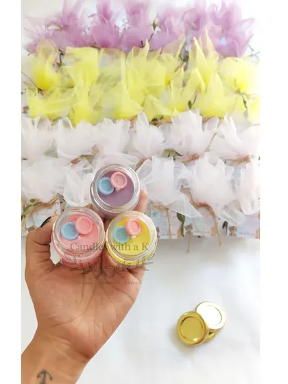 An order of personalized baby shower return gifts, featuring mini scented jar candles with cute button toppers in various pastel colors.