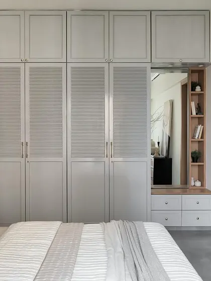 Custom-designed wardrobes grace this master bedroom. One half showcases louvers, while the other has a sleek matte grey PU finish, with an integrated vanity nook for added functionality.