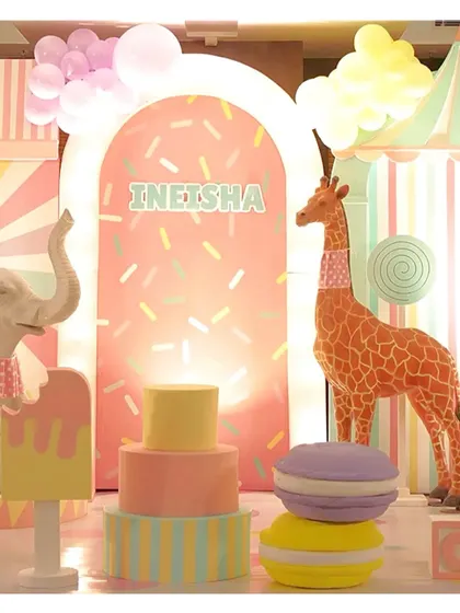 A close-up of the candyland setup, with a tall giraffe prop, a tiered cake, and a giant macaron, all in soft pastel colors.