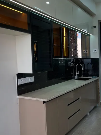 This is a completed project featuring our popular beige high-gloss handleless cabinets. The design includes black-tinted glass upper cabinets and integrated lighting for a premium look.