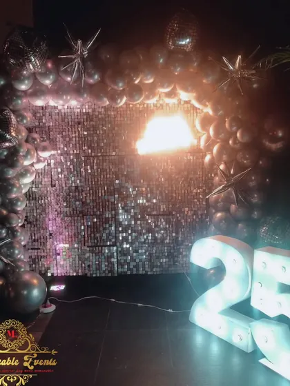 A glamorous 25th birthday setup with a silver shimmer wall and starburst foil balloons.