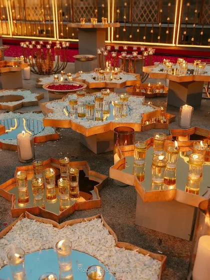 Mirrored tables are filled with flower petals, candles, and shot glasses, creating a sea of light around the Varmala stage.