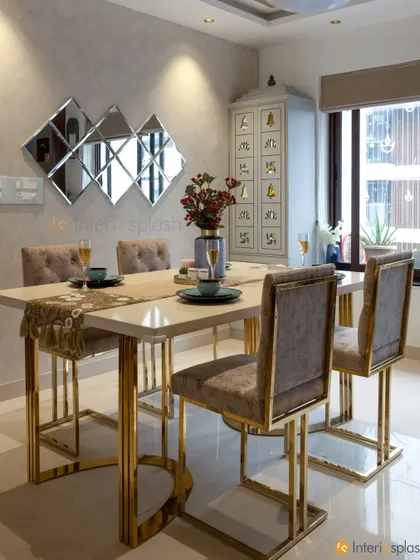 This luxurious dining room features a marble-top table with striking gold-finished legs and plush, high-back chairs. The mirrored wall decor adds a touch of glamour and reflects light beautifully.