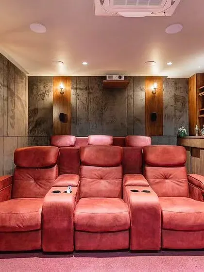 A cozy home theater setup with plush red recliner seats and acoustic wall paneling. A built-in bar unit at the back makes it the perfect space for movie nights.