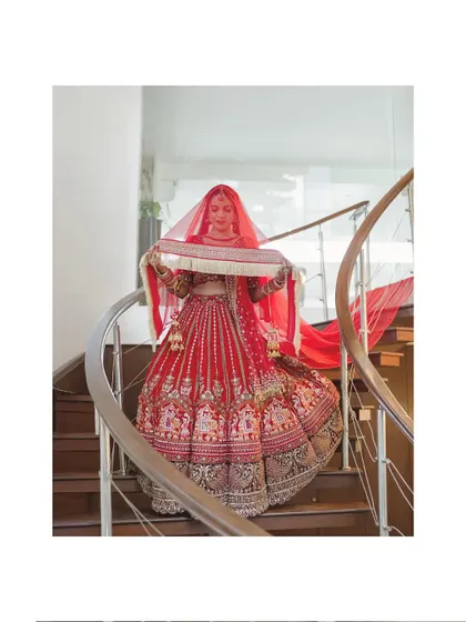 The bride descends a spiral staircase, her red lehenga and veil creating a stunning visual.