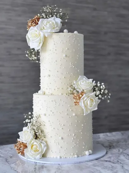 A classic and timeless two tier wedding cake. The simple design with pearl dot details is elevated by clusters of beautiful white roses, creating a look of pure elegance.