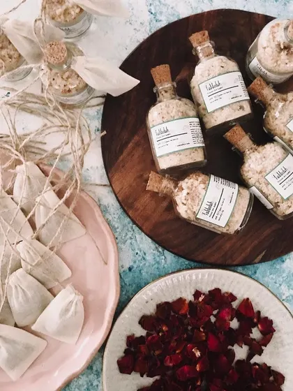 A beautiful flat-lay of a bath salt order being prepared. You can see the individual bottles, the muslin bags, and a plate of dried rose petals which I often include in my blends.