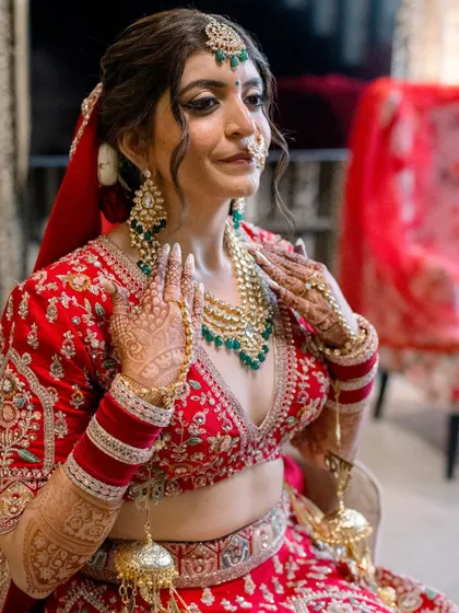 Divya looking like a queen. The soft smokey eye and flawless skin pair beautifully with her intricate red lehenga and green jewelry.
