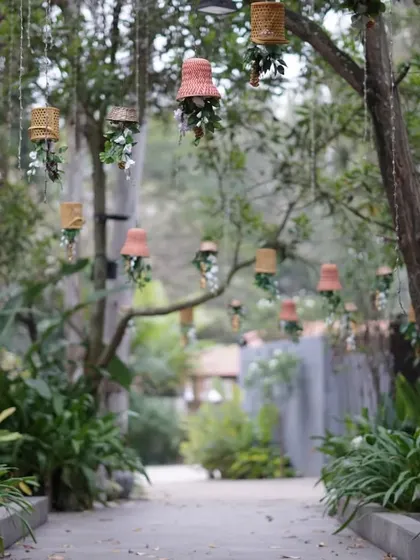 A whimsical pathway decorated with small hanging floral arrangements suspended from tree branches, creating an enchanting entrance for guests.