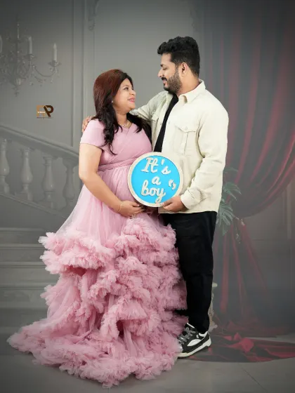 It's a boy! The happy couple announces their baby's gender with a cute sign. The mom-to-be's soft pink gown and the classic studio setting create a timeless announcement photo.