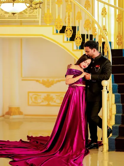 An intimate moment on a grand staircase, with the groom kissing the bride's forehead as her long magenta gown trails down the steps.