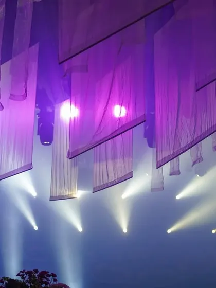 An abstract ceiling view from an evening event at the same location, where beams of light cut through hanging white fabrics, creating a dramatic and modern effect.