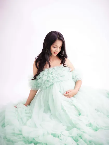 A soft and delicate portrait. The mom-to-be is seated in a cloud of mint green tulle, her expression gentle and serene.