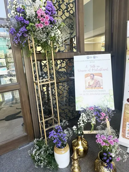 The entrance to the spiritual event, featuring a welcome sign for "A Talk on Women of Mahabharat," flanked by elegant floral arrangements that set a respectful and serene tone.