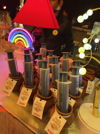 A fun and interactive serving idea for a birthday party. These are cocktail shots served in syringes, placed in traditional clay kullads with personalized 'Happy Birthday' tags.