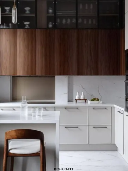 This modern kitchen design balances textures beautifully, with vertically fluted wood upper cabinets, sleek white lower cabinets, and a clean white countertop that extends into a breakfast bar.
