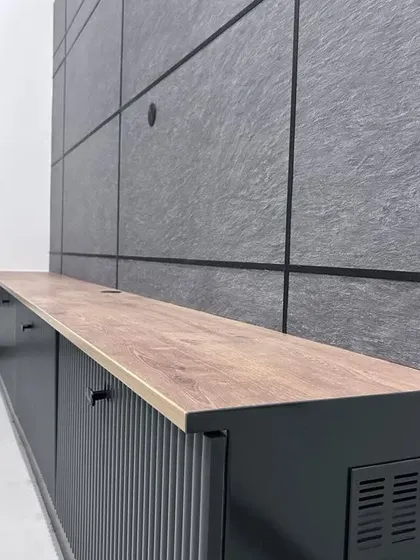 A close-up of a fluted TV console set against a textured grey wall panel. This detail shot highlights our focus on material quality and contemporary design trends.