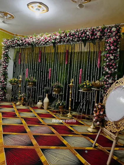 An elegant naming ceremony setup with a backdrop of hanging jasmine garlands. The stage is decorated with brass lotus stands, a traditional lamp, and a custom welcome mirror.