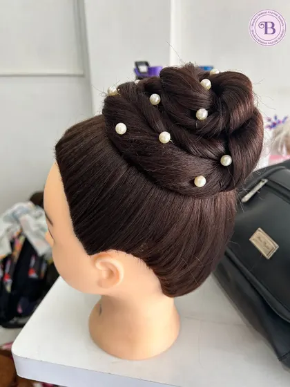 An elegant high bun with intricate weaving and pearl details. This is a classic bridal hairstyle that my students learn to perfect.