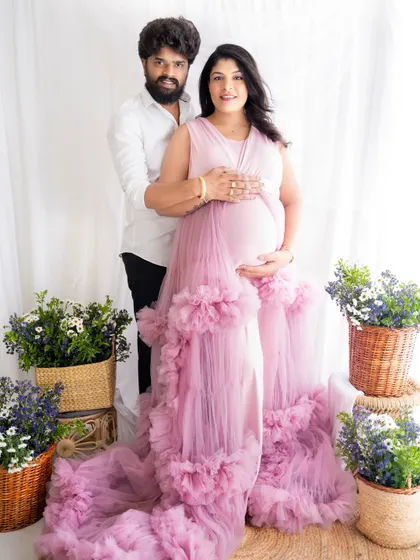A classic and happy portrait of an expecting couple standing together, surrounded by flowers, looking at the camera.