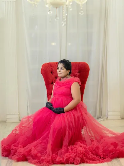 An elegant, regal portrait of a mom-to-be seated in a throne-like chair, wearing a beautiful red gown and gloves.