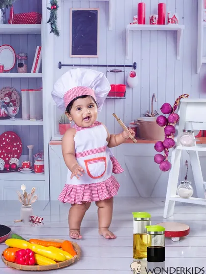 Another adorable little chef in the studio kitchen. Dressed in a pink and white apron, she's ready to get cooking with her rolling pin, creating a fun and playful scene.