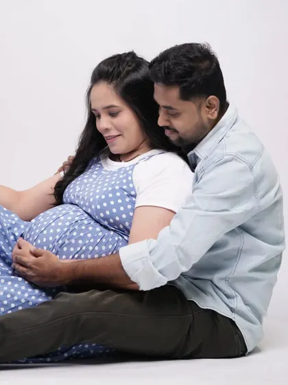 A candid and loving moment on the studio floor. The couple shares a look while cradling the baby bump, creating a relaxed and intimate portrait.