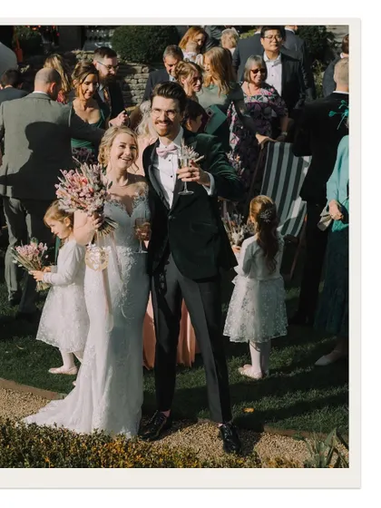 The bride and groom raise their glasses to the camera, a cheerful and engaging portrait from their garden reception.