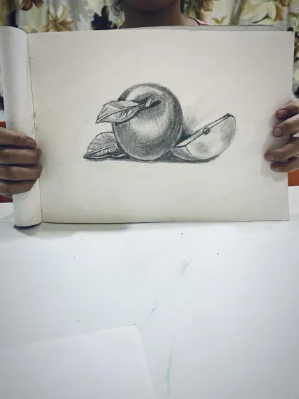 A student proudly shows their still life drawing of an apple, done with beautiful, soft shading.