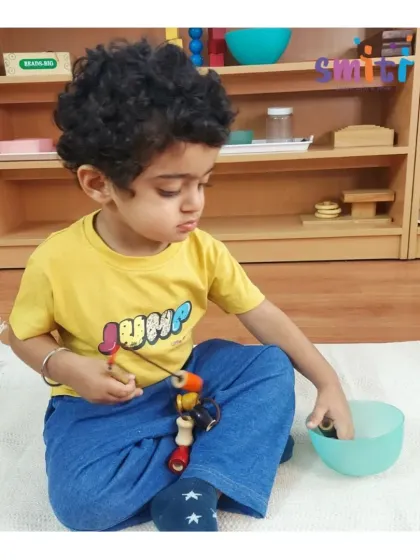 With focused attention, a toddler threads large wooden beads onto a string. This is an excellent exercise for developing fine motor control and hand-eye coordination.