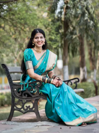 A full-length portrait of the bride seated on a park bench, showcasing her elegant turquoise saree and relaxed smile.