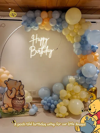 A "pooh-tiful" first birthday setup for little Anaya. This Winnie the Pooh theme featured a round backdrop with a neon "Happy Birthday" sign, surrounded by pastel blue and yellow balloons.