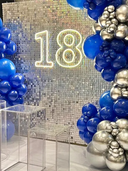 An 18th birthday celebration with a glamorous silver sequin wall and a bold blue and silver balloon arch. The neon "18" makes it a perfect centerpiece for this major milestone.