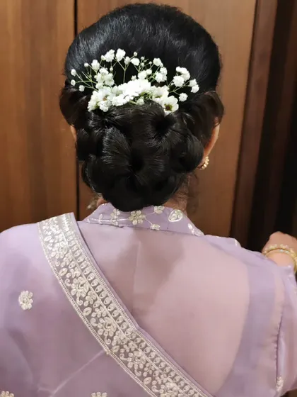 A classic, intricate braided bun adorned with baby's breath. This is a timeless hairstyle for wedding guests, pairing beautifully with a traditional saree.