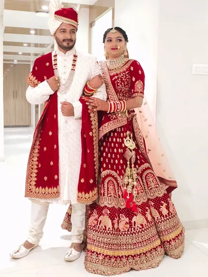 This full-length shot shows how the groom's white and red sherwani is perfectly complemented by the bride's red lehenga. A coordinated look makes for stunning wedding photos.