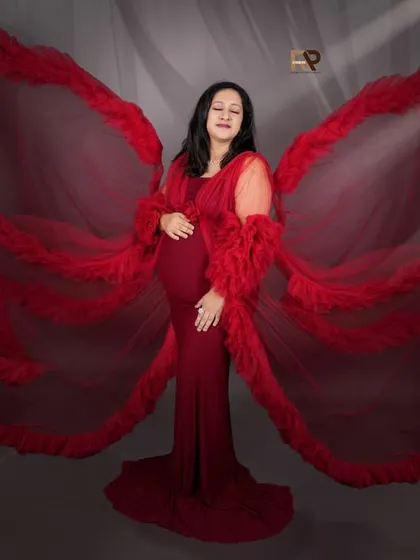 A dramatic and artistic pose. The red gown's fabric is fanned out like wings, creating a powerful image that is enhanced by ethereal light beams.