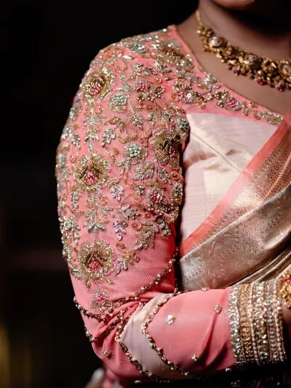 A close-up of the sleeve of a peach organza blouse. The entire sleeve is heavily embroidered with zardosi, beads, and threadwork, creating a rich and luxurious texture that feels incredible to wear.