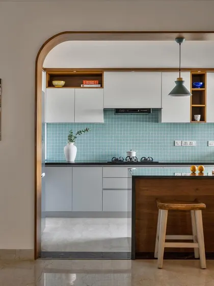 This open-plan kitchen features an arched pass-through, a teal tile backsplash, and a wooden breakfast bar that connects it to the dining area.