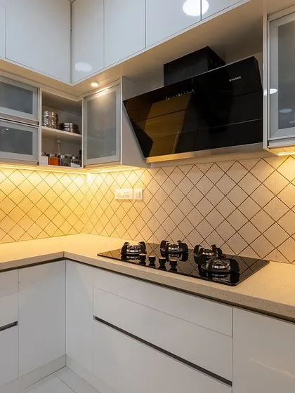 A bright and modern kitchen with white cabinets and frosted glass doors. The diamond-patterned backsplash and under-cabinet lighting add a touch of warmth and texture.