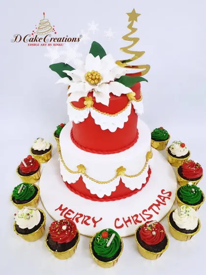 An elegant Christmas cake and cupcake set. The two-tier cake in red and white is adorned with a beautiful sugar poinsettia, while the matching cupcakes create a festive display.