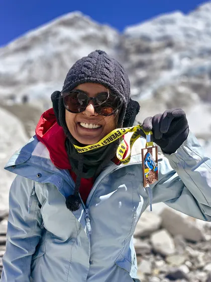 The smile of success at Everest Base Camp. A trekker proudly displays her completion medal with the formidable Khumbu Icefall in the background, a testament to her hard work and determination.