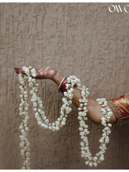 A detail shot of the bride's hand, adorned with henna, holding a string of fresh jasmine flowers.
