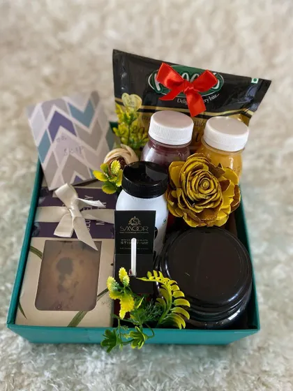 This care hamper combines healthy and indulgent items. It features fresh juices, a slice of cake, and other snacks, decorated with yellow flowers to create a bright and cheerful gift for any employee.