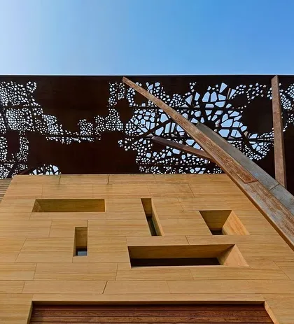 A low-angle view of the Tree House, emphasizing the tree-like columns that support the perforated roof. The geometric cutouts in the stone facade below add another layer of detail and control the light entering the home.