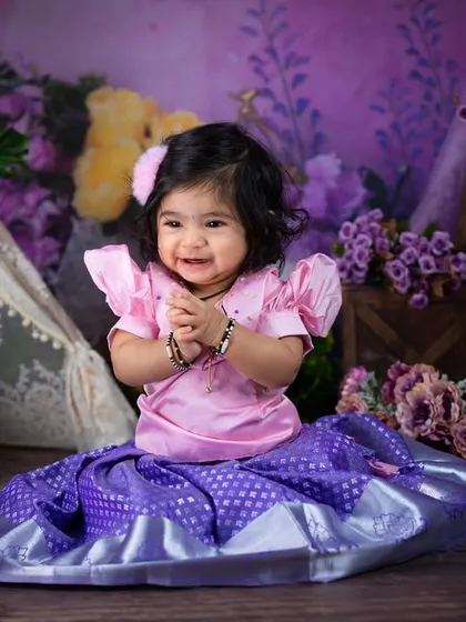 A sweet, clapping gesture from a little girl in a lovely pink and purple traditional outfit. The lavender-themed background complements her dress perfectly.