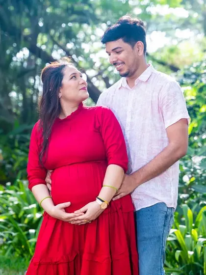 A change of outfit to a vibrant red dress brings a different energy to the photoshoot. This image captures a warm, loving embrace amidst the lush greenery.
