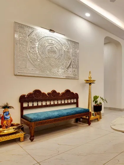 A traditional carved wooden bench with a bright blue cushion, paired with a brass lamp and a stunning silver-foiled wall art piece, blending heritage with luxury.