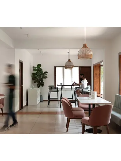 A view of the upper floor's community table, featuring a long wooden live-edge surface. This area is designed for small informal meetings or gatherings, overlooking the lush green surroundings through a large window.