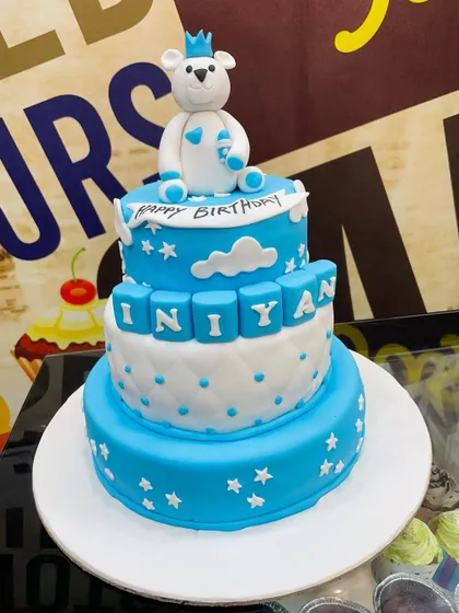 A grand 6kg three-tiered cake for a first birthday, in blue and white with a teddy bear king on top.