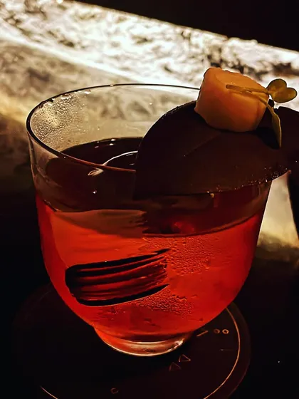A creative twist on a classic Negroni. The drink is garnished with a disc of dark chocolate and a piece of candied fruit, adding notes of bitterness and sweetness.